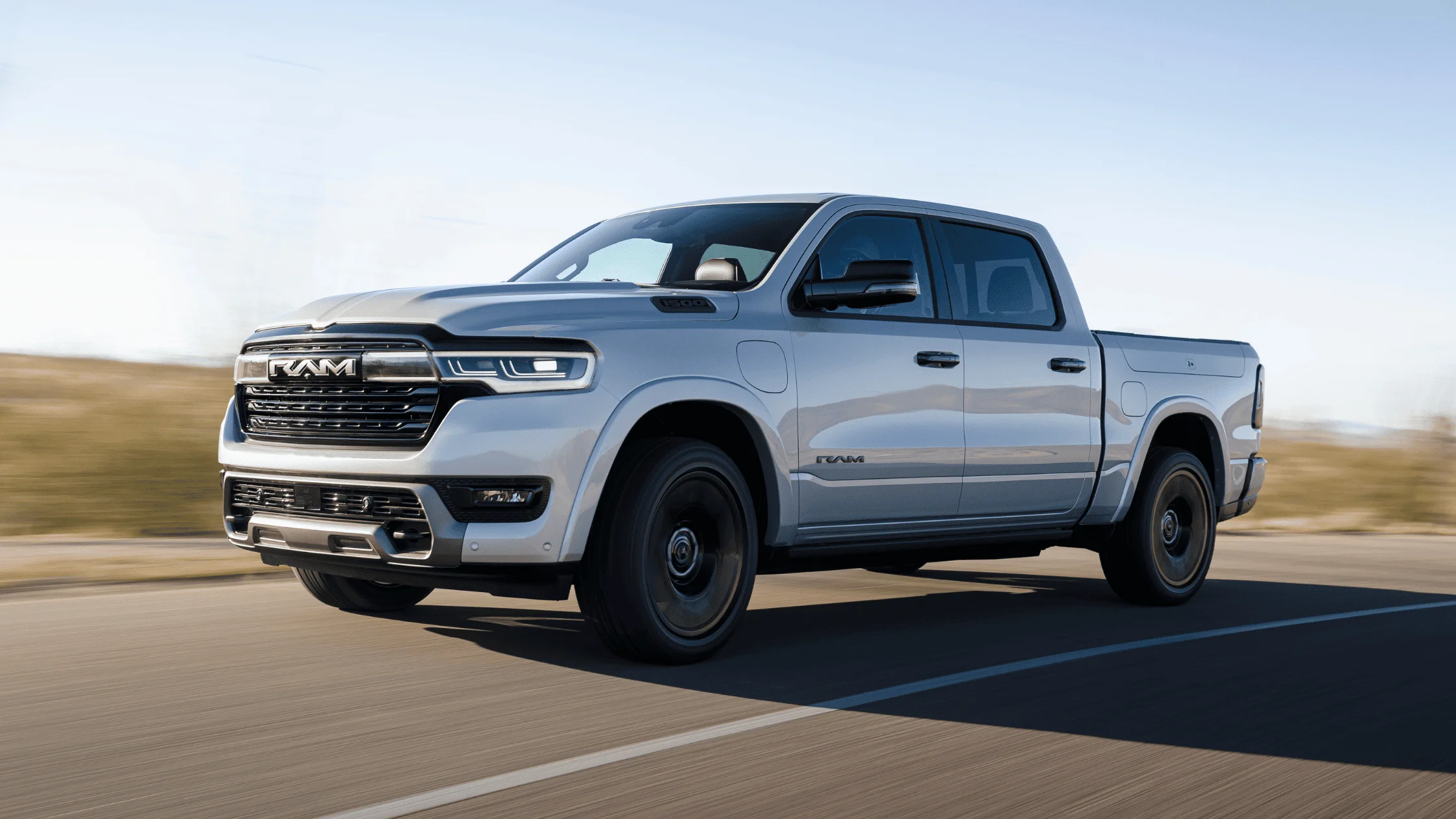 Silver 2026 Ram 1500 REV electric truck driving on a clear highway, showcasing its aerodynamic front grille and modern LED lighting design.