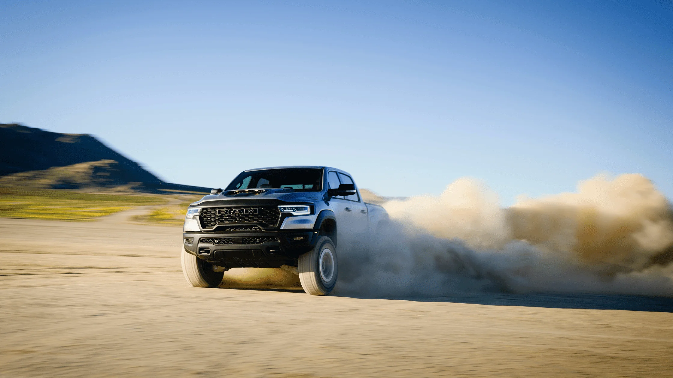 2025 Ram 1500 RHO kicking up dust while drifting on desert trail under clear blue sky