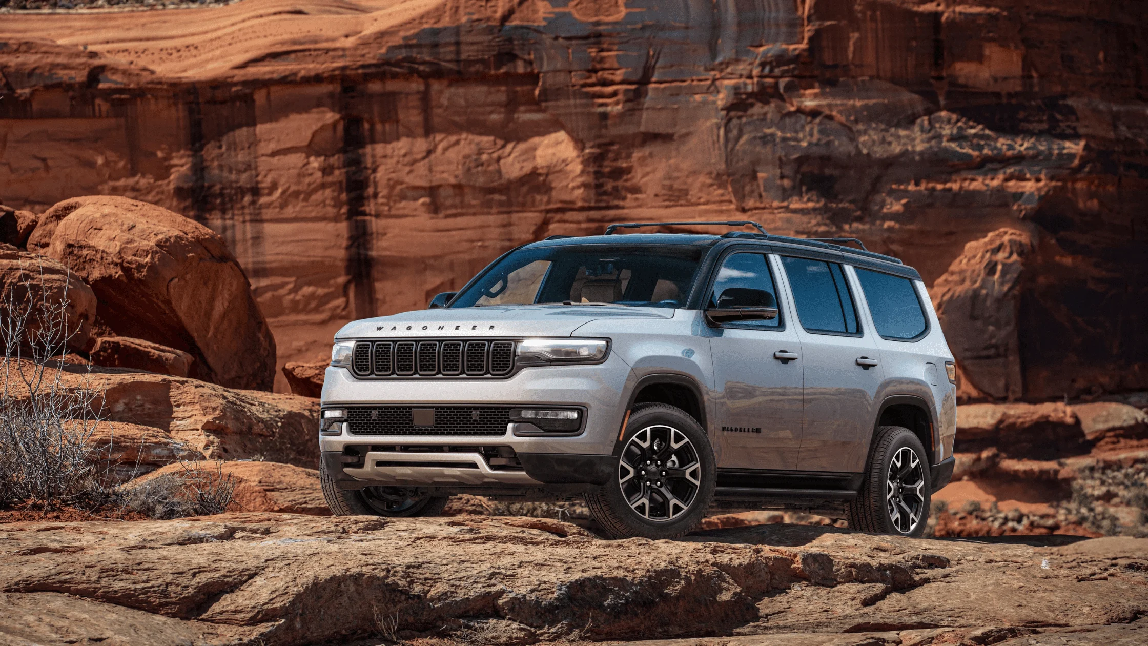2025 Jeep Wagoneer in silver parked on rocky terrain with red sandstone cliffs in the background
