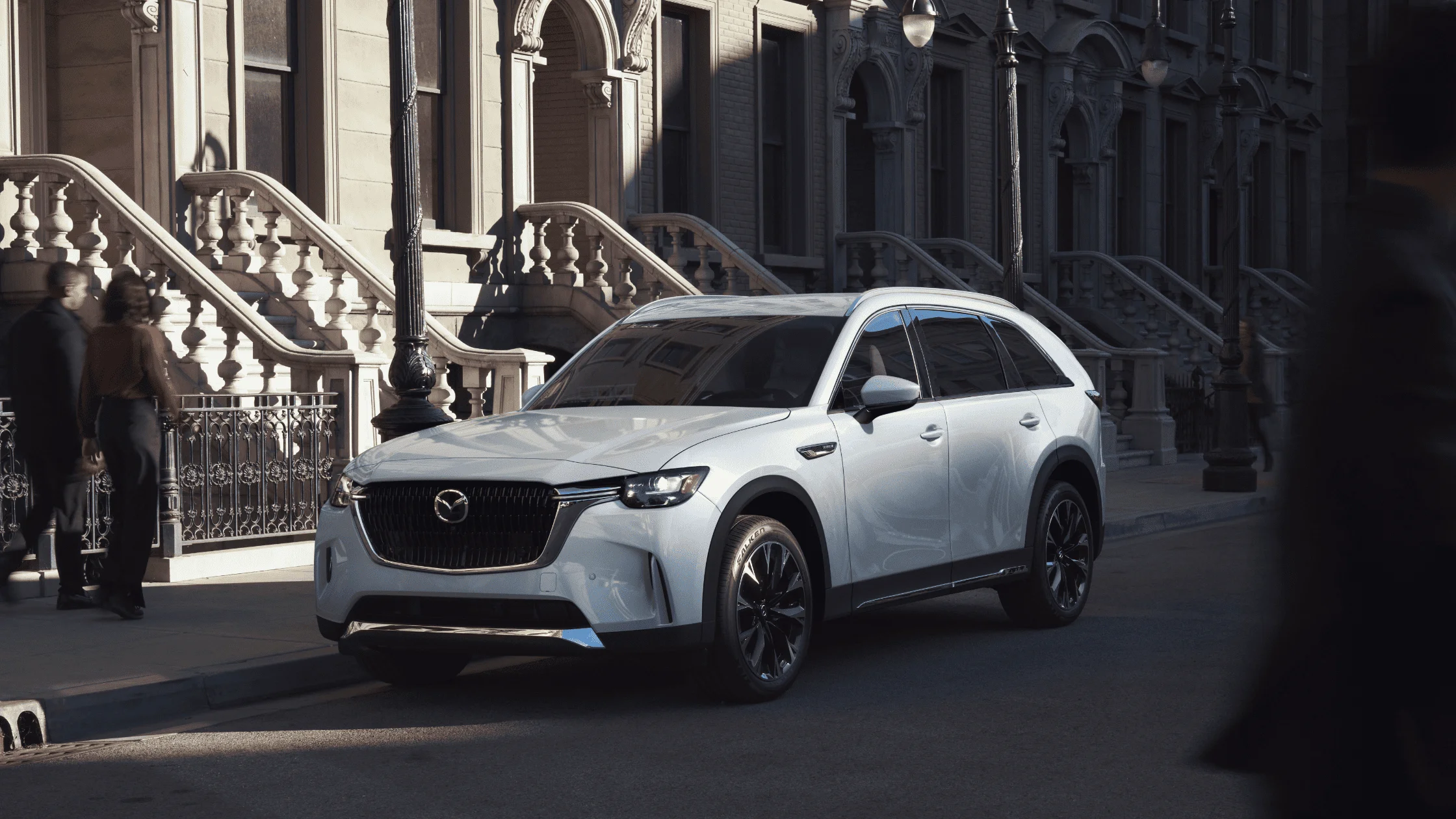2025 Mazda CX-90 in white parked curbside in front of brownstone buildings with pedestrians nearby