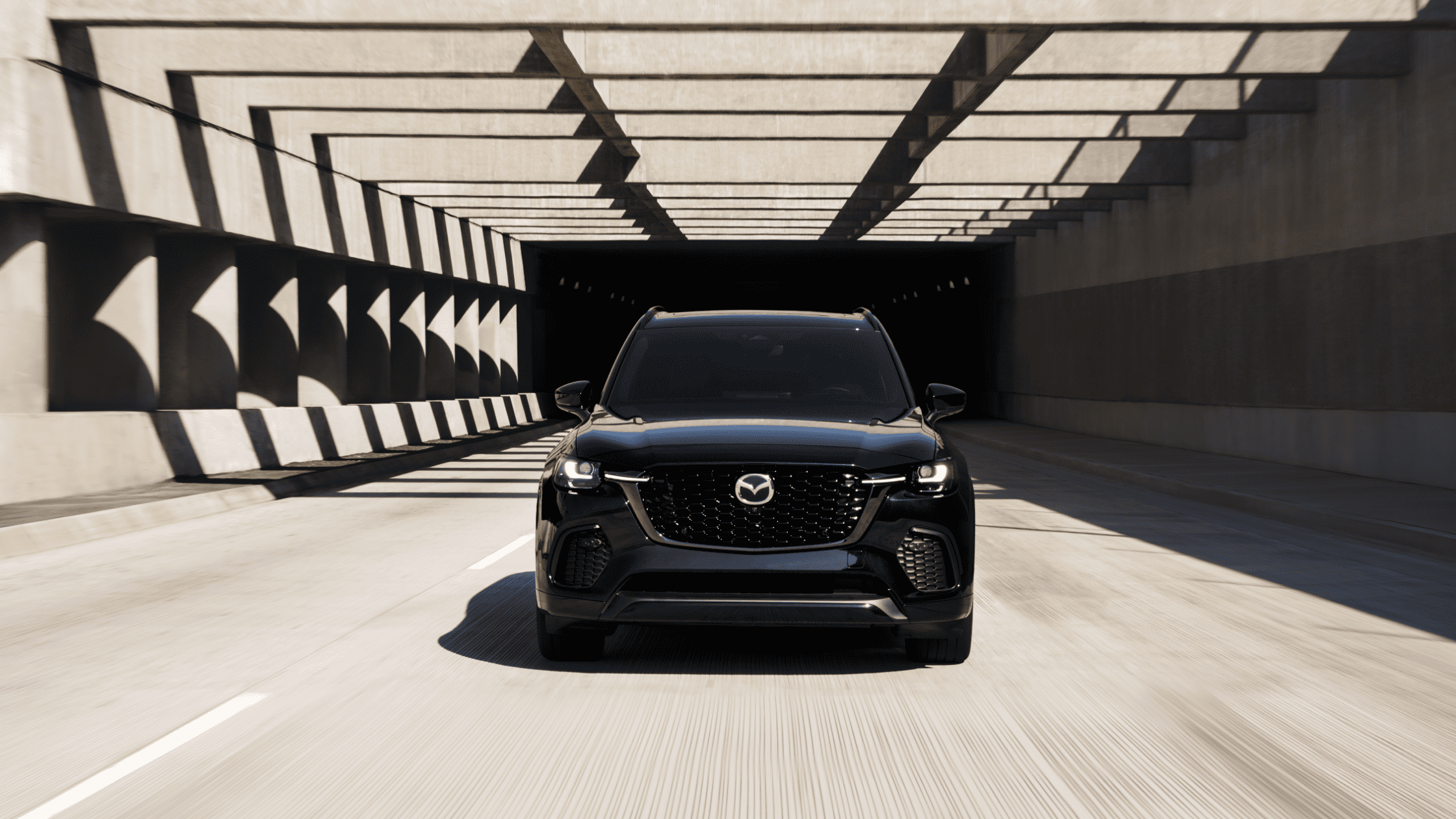 Black Mazda CX-70 PHEV SUV front view, tunnel backdrop, exterior daylight setting