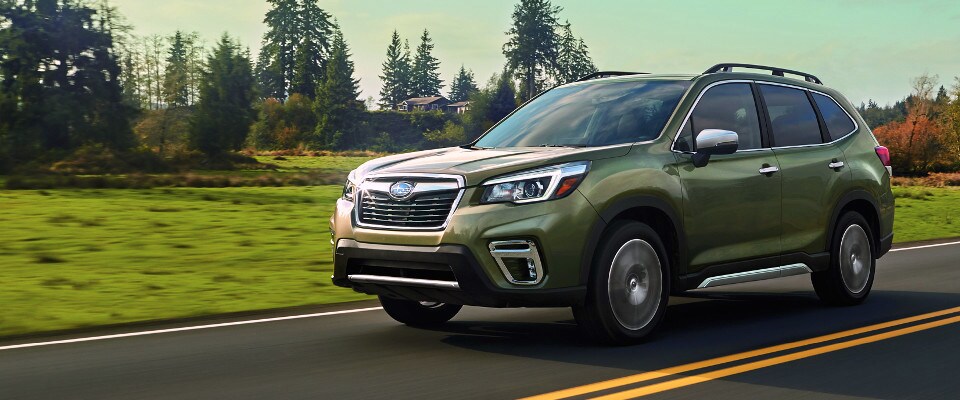 A green 2019 Subaru Forester driving down an open country road