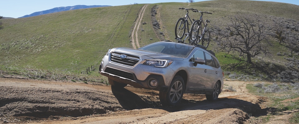 Silver 2019 Subaru Outback driving up a dirt hill with two bikes