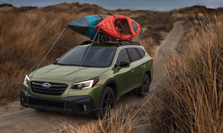 2020 Subaru Outback in green driving on a dirt path with kyaks straped to the top
