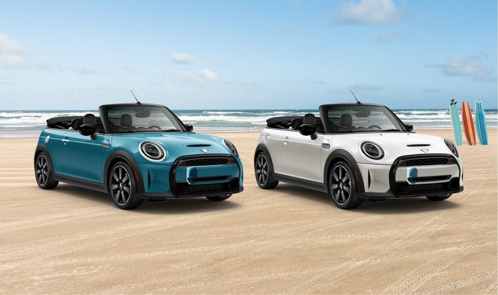 Three-quarters front view of a MINI Cooper S Convertible Seaside Special Edition in Caribbean Aqua parked on a beach next to a MINI Cooper S Convertible Seaside Special Edition in Nanuq White, with crashing waves and clear skies in the background.
