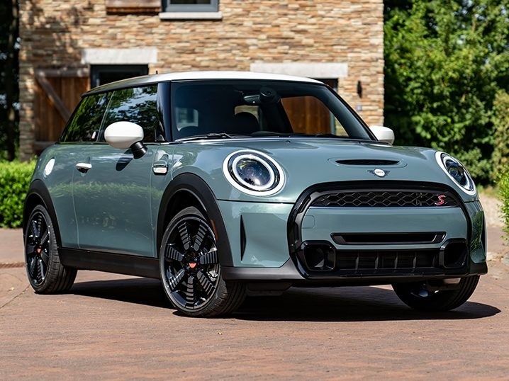 Three-quarters view of a MINI Hardtop 2 Door Multitone Edition in Sage Green parked on a brick surface.