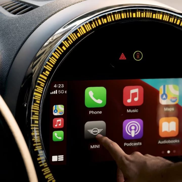 Closeup view of the touchscreen media display in a MINI vehicle, with a person's index finger pointing at the MINI application button on its screen.