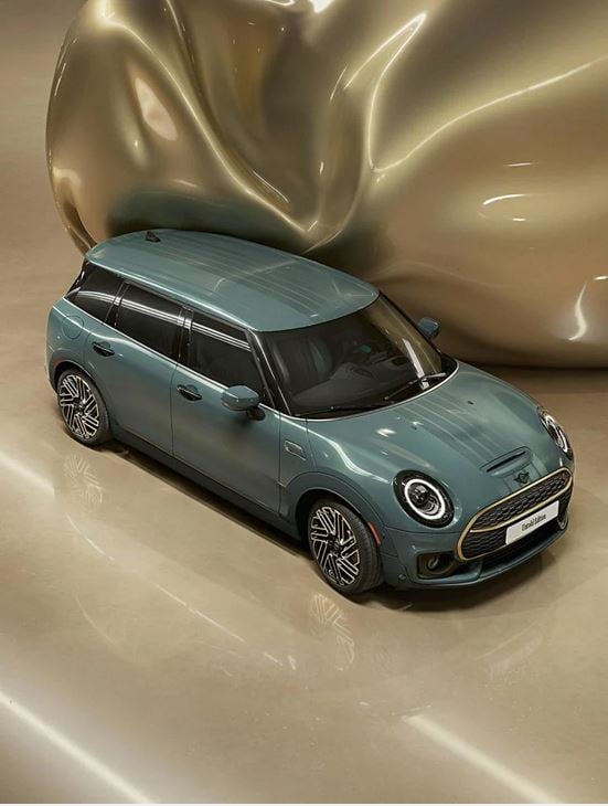Three-quarter top view of the refined brass front and rear accents on a MINI Clubman Untold Edition, which has a giant CGI, inflating, shiny, brass balloon coming from the side of the car.