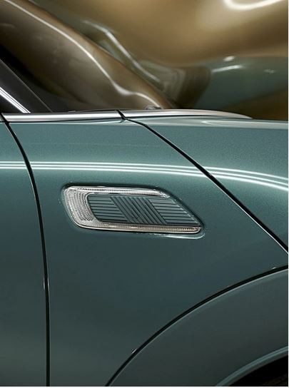 Closeup of the Sage Green metallic paint with piano black exterior trim on a MINI Clubman Untold Edition with a giant CGI, inflating, shiny, brass balloon coming from the side of the car.