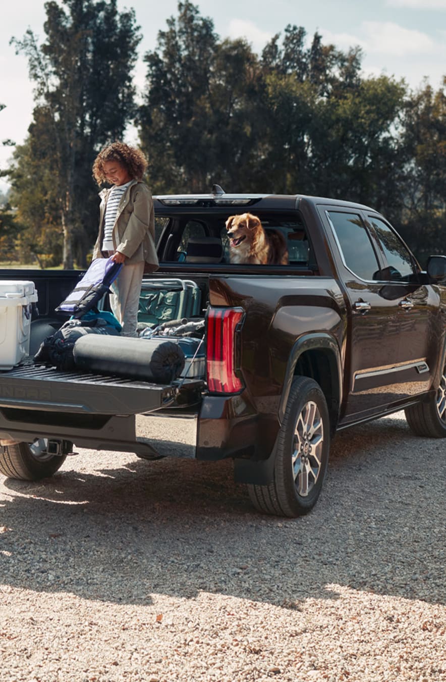 The New 2023 Toyota Tundra at Mechanicsville Toyota in Mechanicsville, VA | Rear view of a black Toyota Tundra with its trunk open filled with items, alongside a kid and dog
