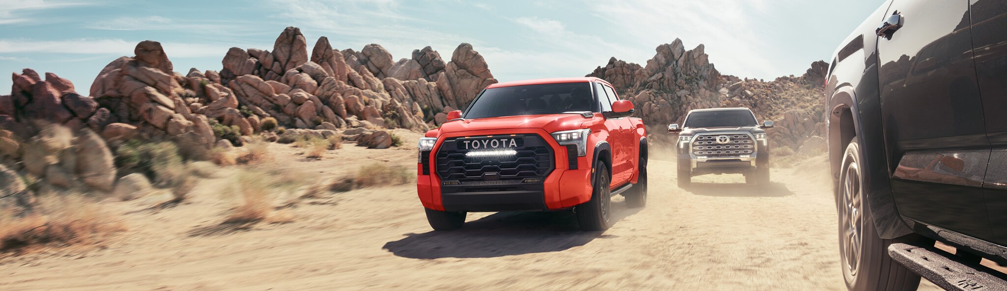 The New 2023 Toyota Tundra at Mechanicsville Toyota in Mechanicsville, VA | Orange Toyota Tundra driving on dirt road while another black Toyota Tundra is right behind it