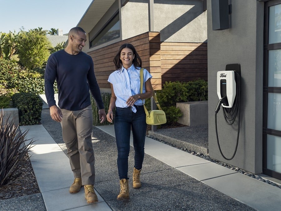 A couple walking out of their home with a Ford Charge Station Pro attached to their garage in the background