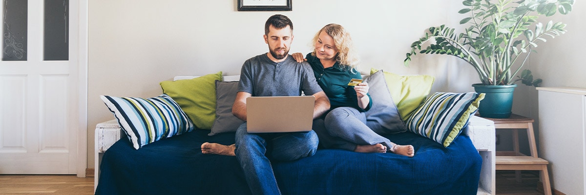 Young couple doing shoppings online on the sofa at home, looking at laptop screen and smiling