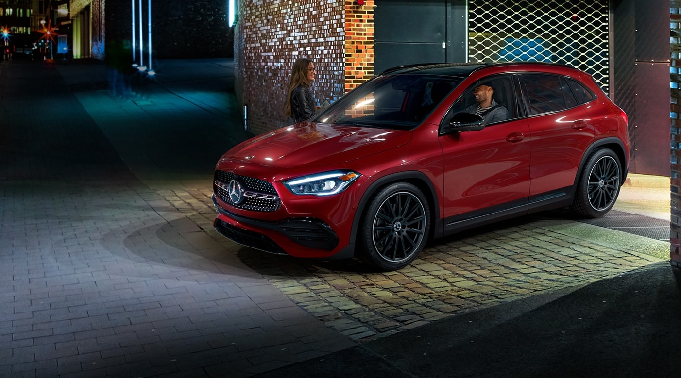 A profile view of a red 2022 Mercedes-Benz GLA as it drives out onto a city street from a parking garage at night