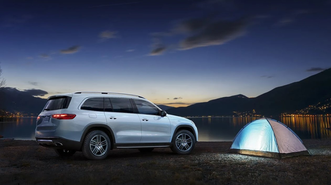 A Mercedes-Benz GLS parked at a lake overnight with a tent set up nearby.