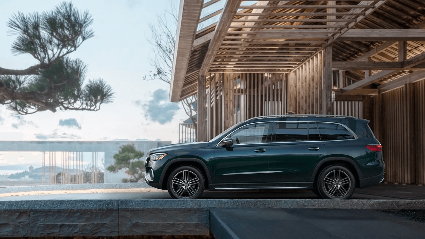 Rendered exterior shot of a Mercedes-Benz GLS SUV parked in front of a wooden structure