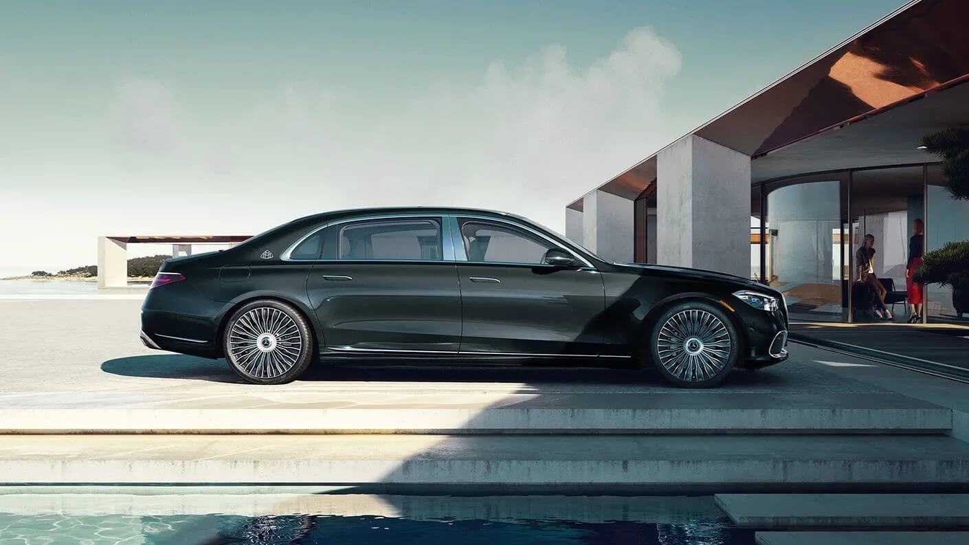 Exterior shot of a Graphite Grey Mercedes-Maybach S-Class parked outside a building with two adult women in the background talking to each other