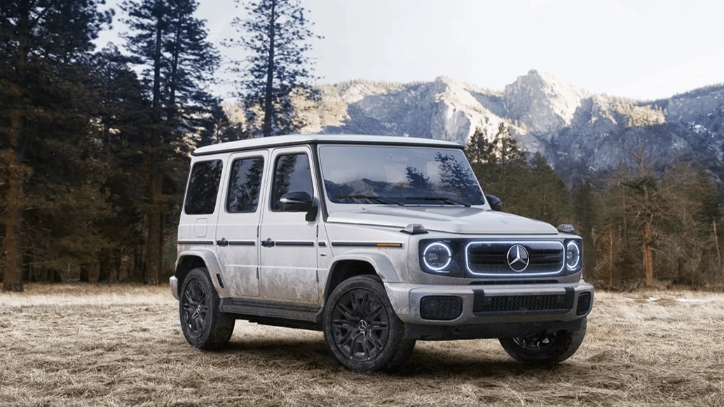 Learn about the off-road capabilities of the Mercedes-Benz G-Class SUV Rendered image of a Mercedes-Benz G-Class SUV parked in a forest setting with a mountain in the background