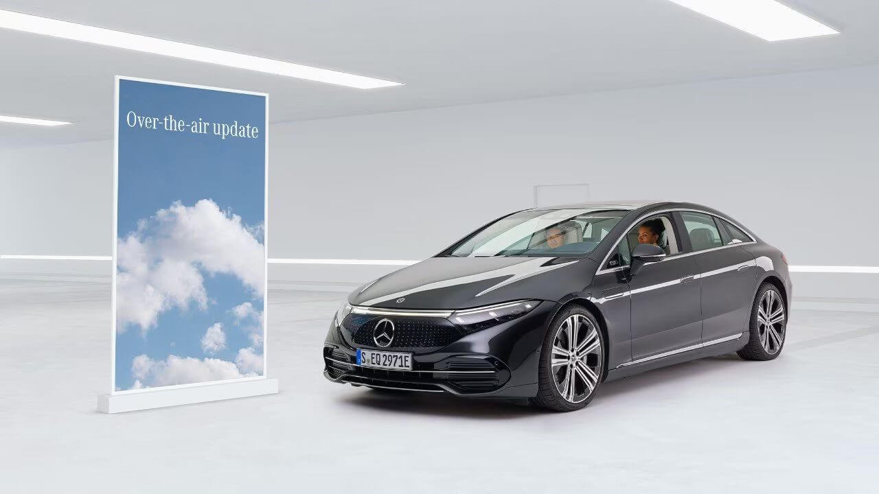 Rendered image of a Mercedes-Benz in an interior showroom parked next to a sign advertising over-the-air updates to the MBUX system
