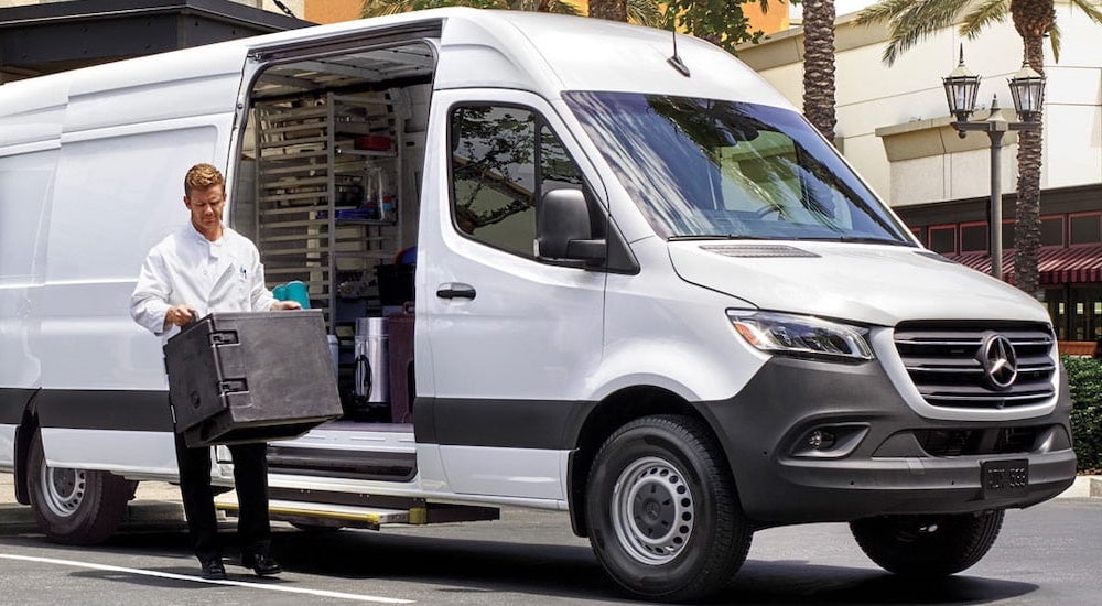 A man carrying a box from the back of a white 2025 Mercedes-Benz Sprinter 2500 for sale near West Chester.