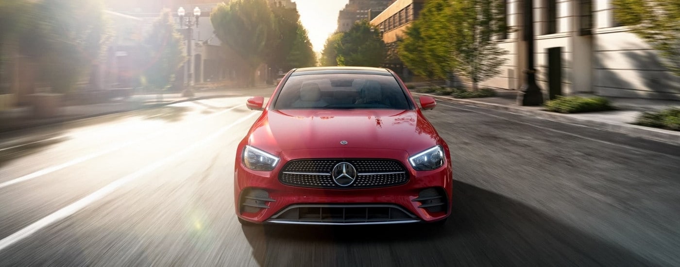 A popular used Mercedes-Benz for sale near Harrisburg, red 2021 Mercedes-Benz E-Class, is shown driving on a city street.