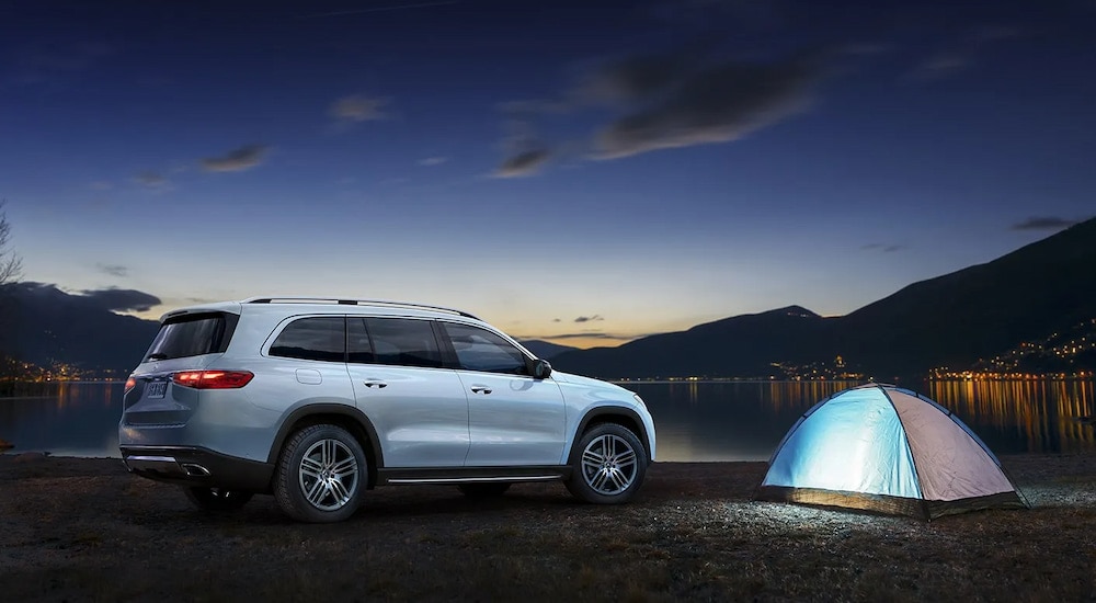 Rear view of a white 2024 Mercedes-Benz GLS 580 parked by a tent at night.