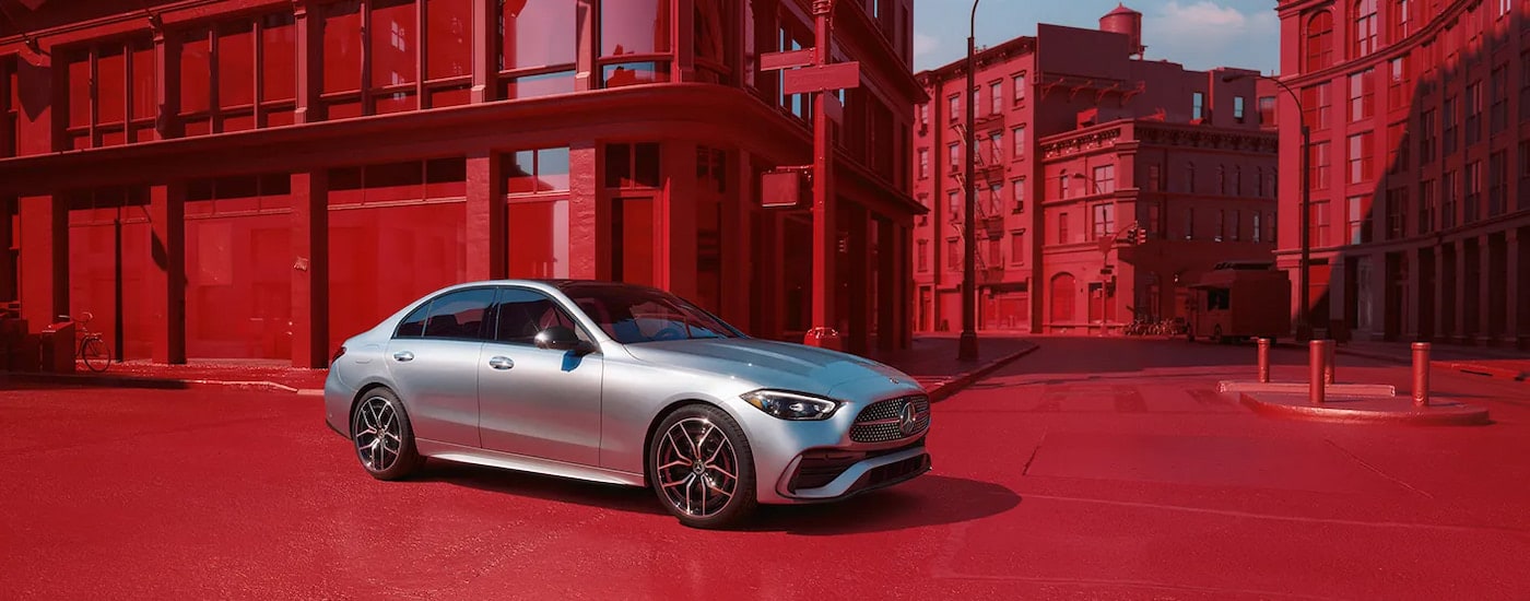 A silver 2023 Mercedes-Benz C 300 driving through a city painted red.