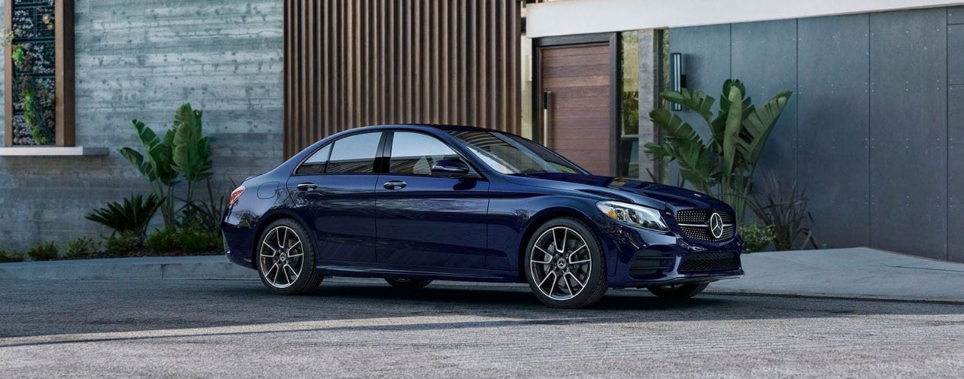 A blue 2020 Mercedes-Benz C-Class for sale is shown parked in front of a modern house.