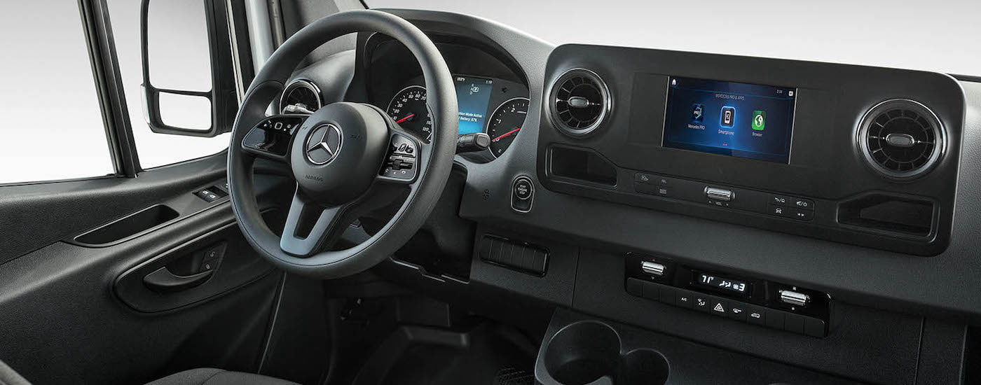 The black interior of a 2024 Mercedes-Benz Sprinter is shown from the passenger side.