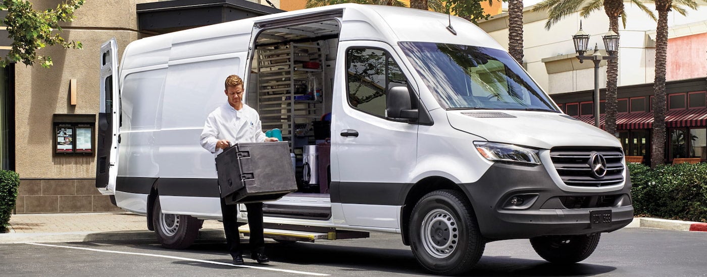 A person loading cargo into the back of a white 2024 Mercedes-Benz Sprinter Cargo Van.