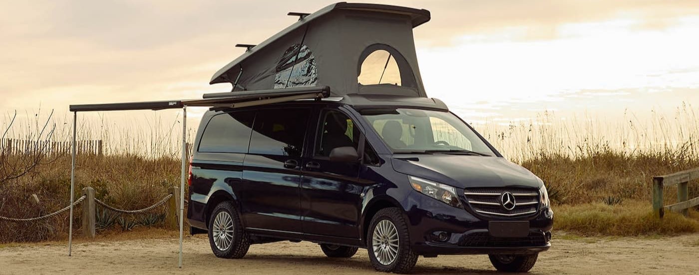 A blue 2024 Mercedes-Benz Metris is shown parked on a campsite.