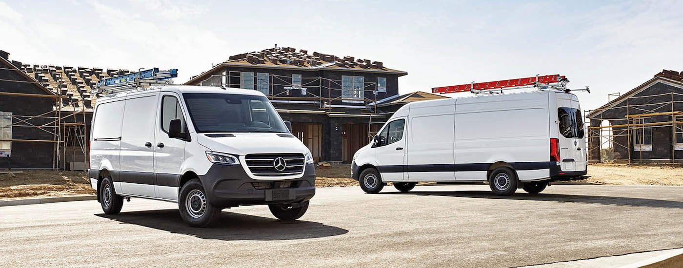 A pair of white 2024 Mercedes-Benz Sprinter Vans are shown parked on a jobsite after leaving a dealer that has a Mercedes-Benz Sprinter 2500 for sale.