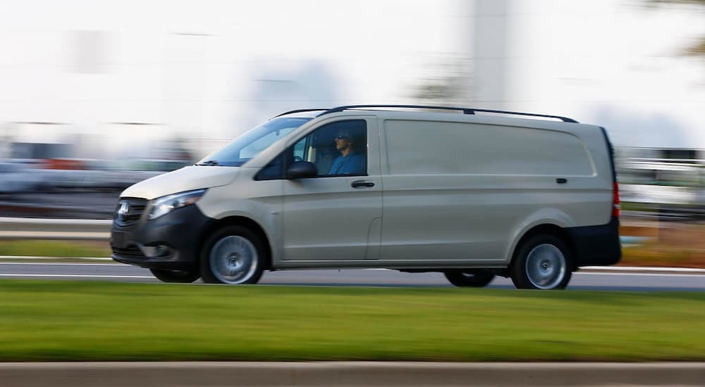 A white 2024 Mercedes Metris is speeding down a city street.