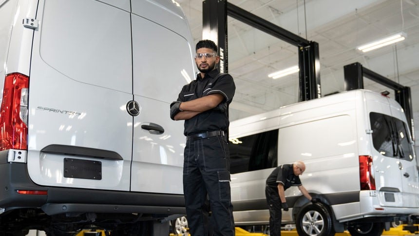 A Mercedes-Benz technician standing behind a Sprinter Van on a lift