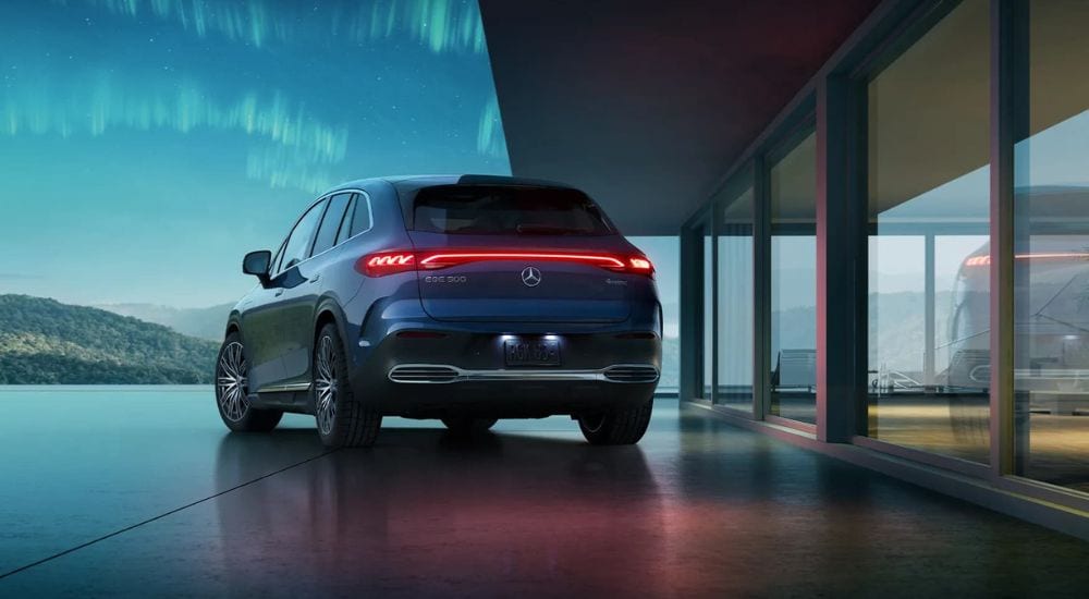 A blue 2023 Mercedes-Benz EQE 500 is shown near a modern house.