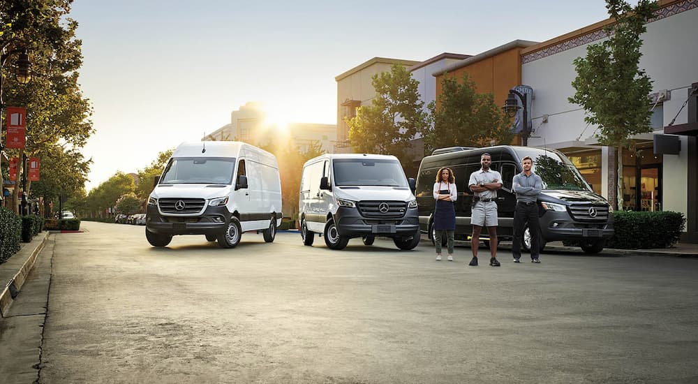 A group of people standing in front of three 2024 Mercedes-Benz Sprinter vans.
