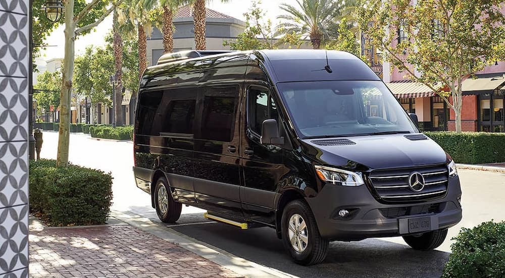 A black 2025 Mercedes-Benz Sprinter 2500 Passenger Van parked by a city curb.
