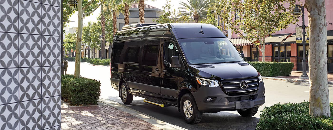 A black 2024 Mercedes-Benz Sprinter Passenger Van parked by a city curb.