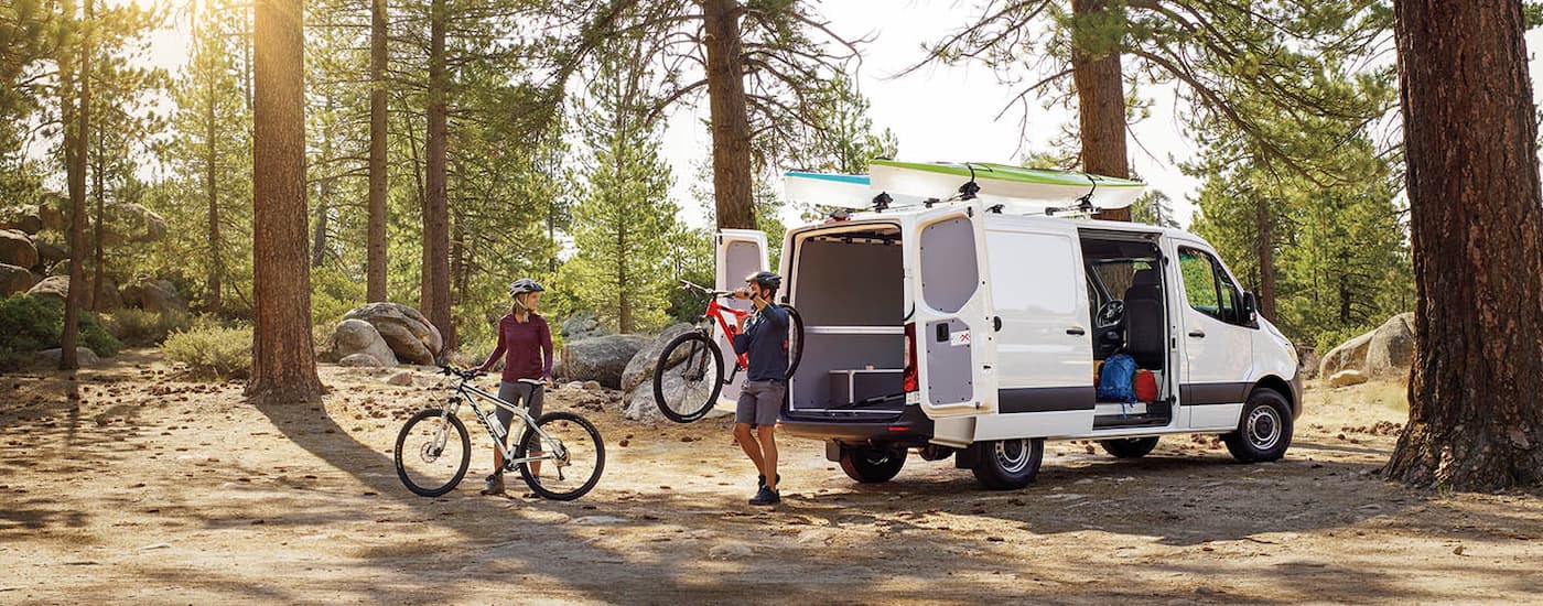 Cyclists unloading bicycles from the open back of a white 2024 Mercedes-Benz Sprinter 4500 Cargo Van.