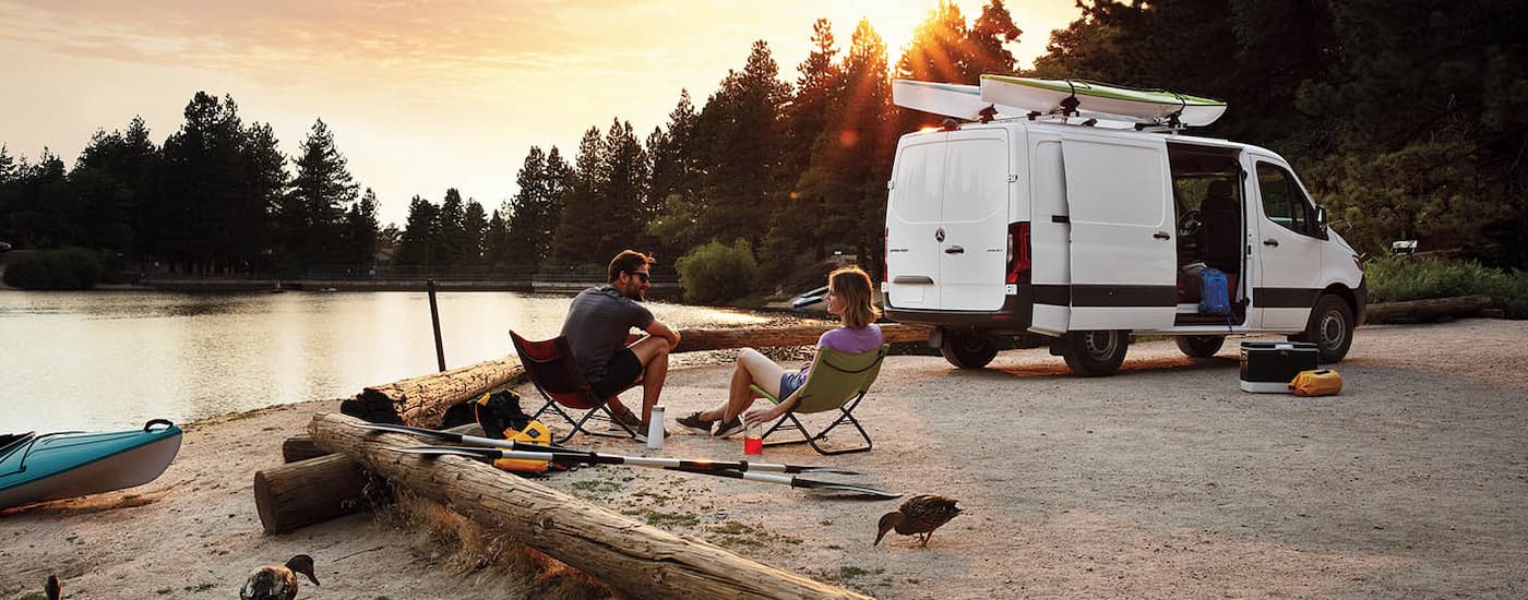 People camping by a lake shore by a white 2024 Mercedes-Benz Sprinter 4500 Cargo Van.