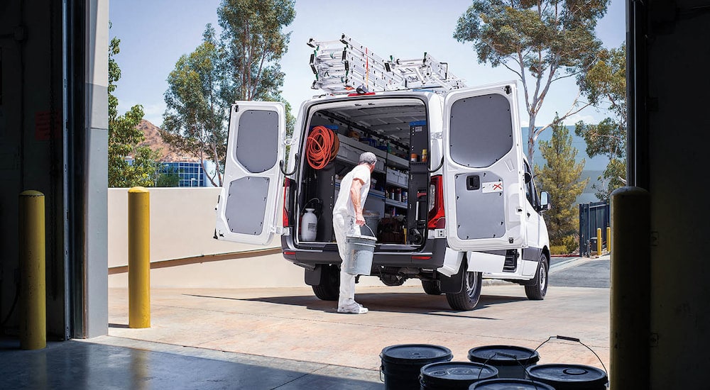 Rear view of an electrician taking gear out of the back of a white 2024 Mercedes-Benz Sprinter Cargo Van.