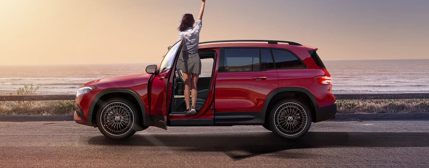 Side angle view of a person waving from the passenger side door of a red 2024 Mercedes-Benz EQB 300 4MATIC.