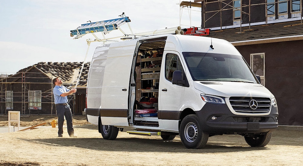 A man unloading a ladder from the roof of a white 2024 Mercedes-Benz Sprinter 2500 cargo van.