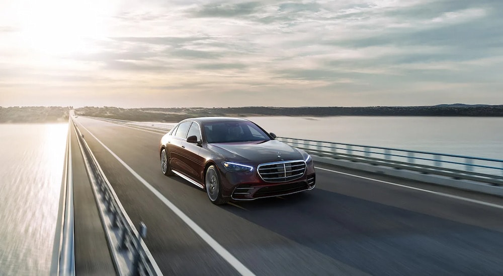 A dark maroon 2024 Mercedes-Benz S 580 AMG Line driving on a bridge.