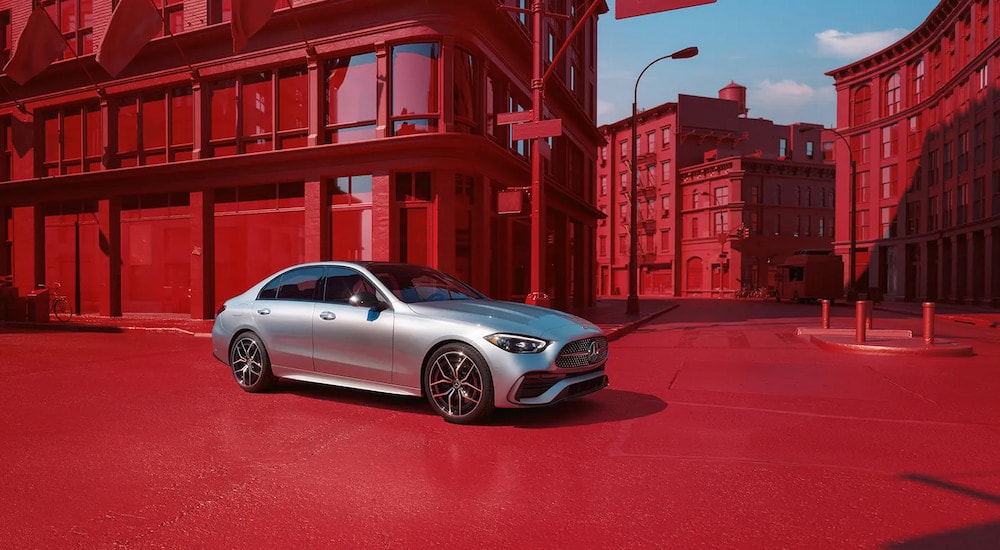 A grey 2024 Mercedes-Benz C 300 Exclusive driving in a red city.