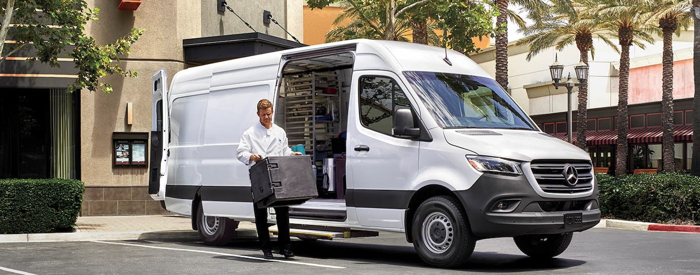 A chef unloading crates from a white 2024 Mercedes-Benz Sprinter 2500 cargo van.