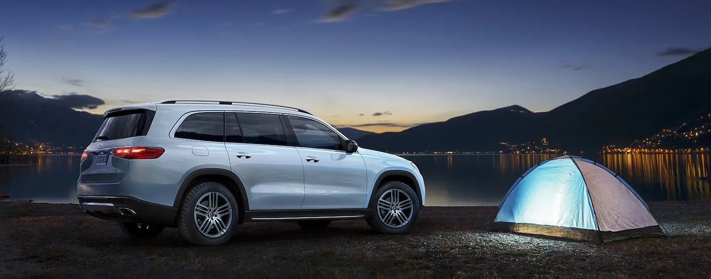 A white 2024 Mercedes-Benz GLS is shown from the side while parked at a campsite.