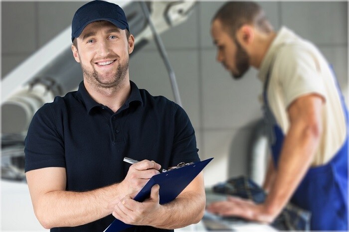 Man_Standing_In_Front_Of_Mechanic_Working_On_Car.jpg