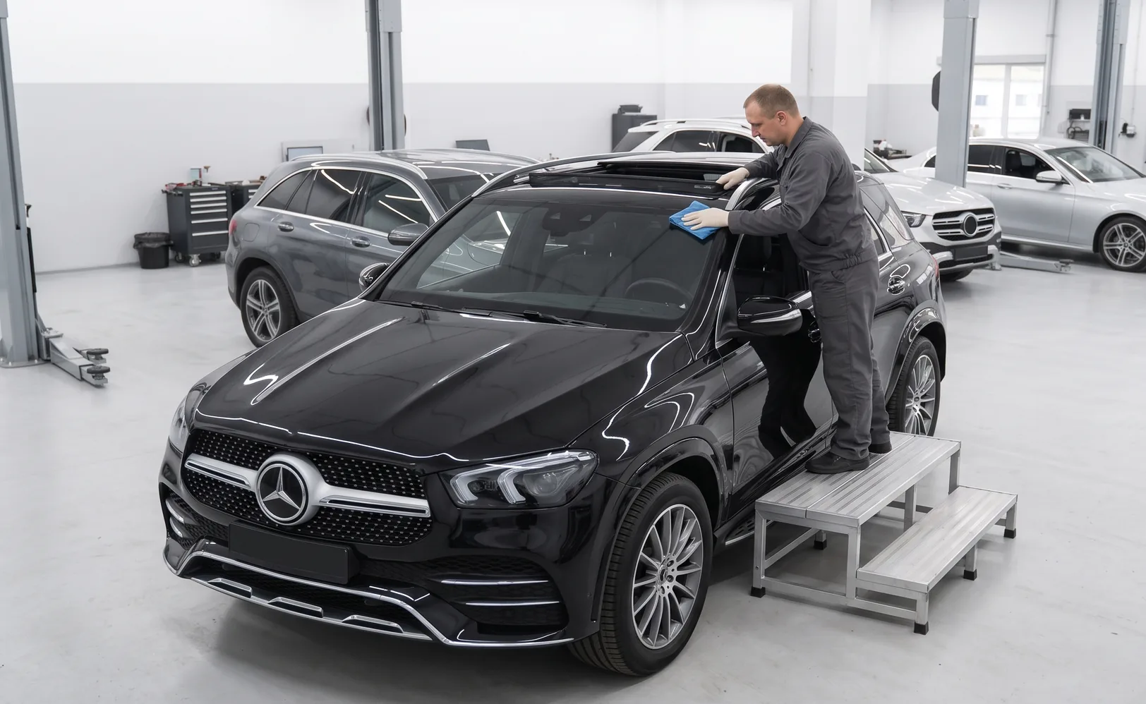 Technician standing on a work platform wiping the sunroof of a black Mercedes-Benz SUV in a service bay