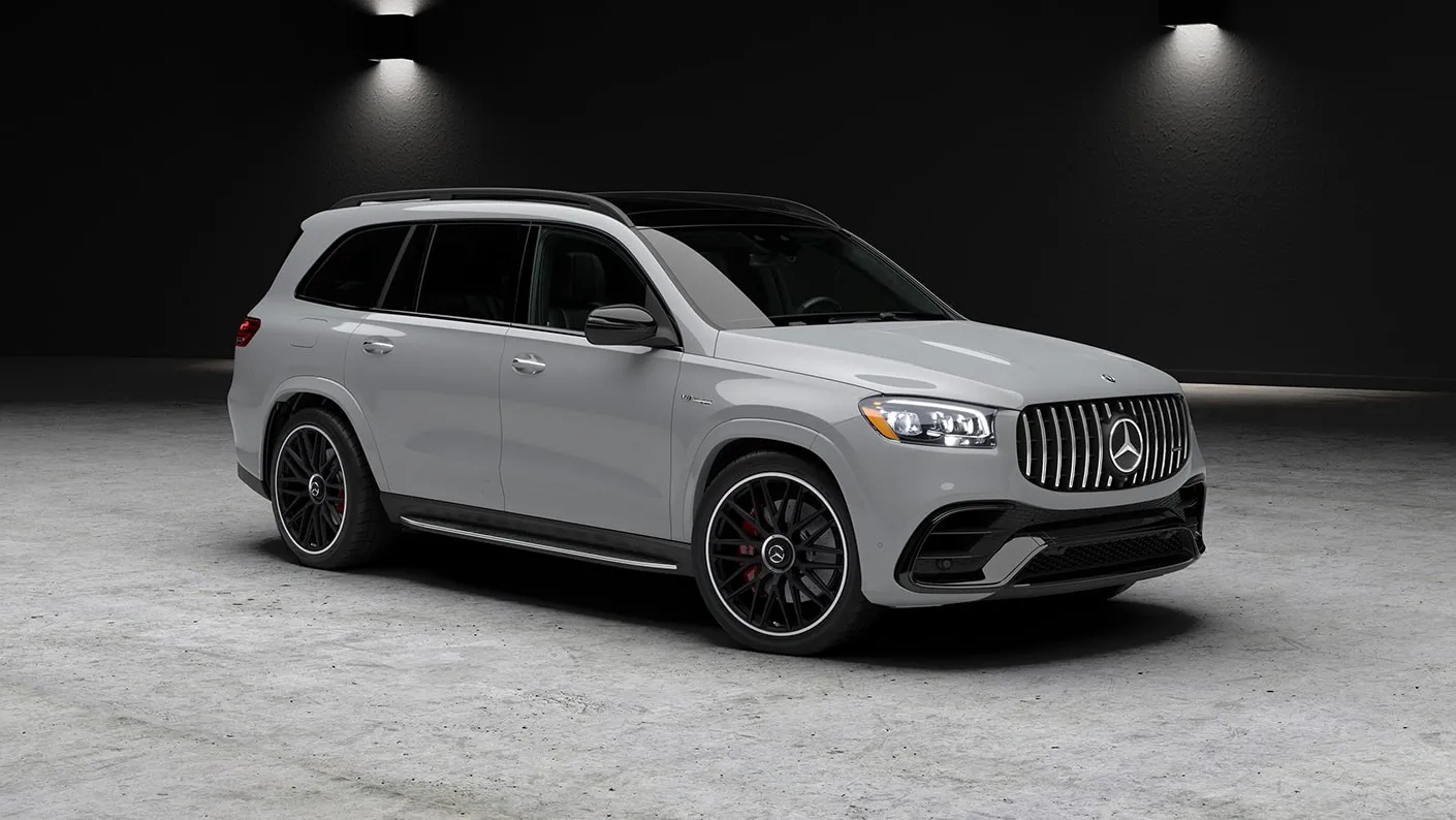 A Mercedes-AMG GLS 63 in light gray, front three-quarter view, lit against a dark studio wall